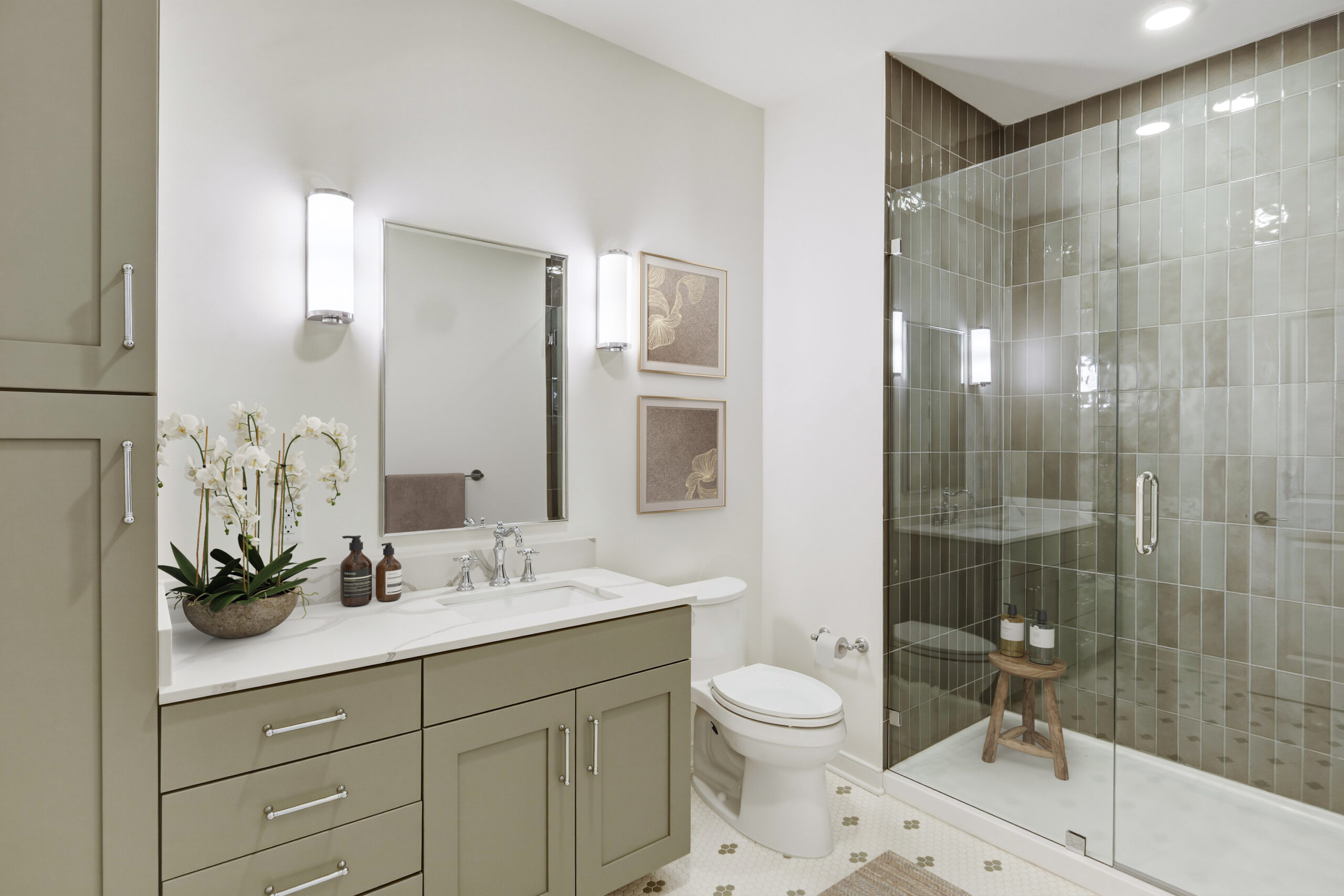 Modern bathroom with a sage green double vanity, white countertop, framed mirror, frameless glass shower, green tiled walls, contemporary lighting, and spa-inspired design.