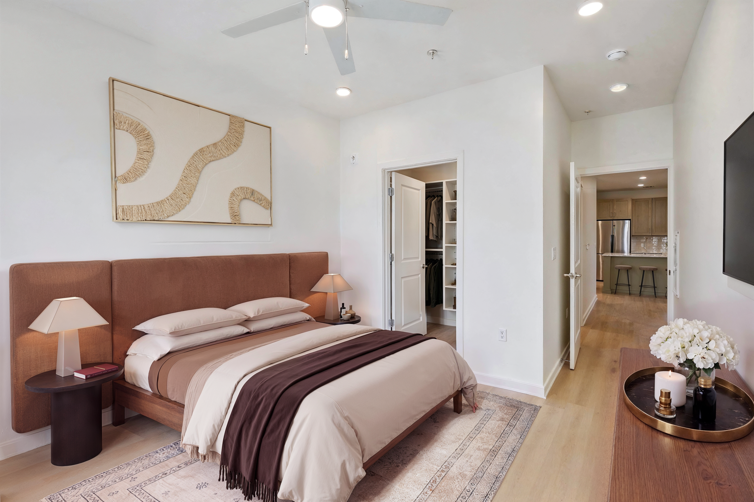Modern bedroom featuring an upholstered brown bed, neutral bedding, wood flooring, contemporary wall art, and bright minimalist décor.
