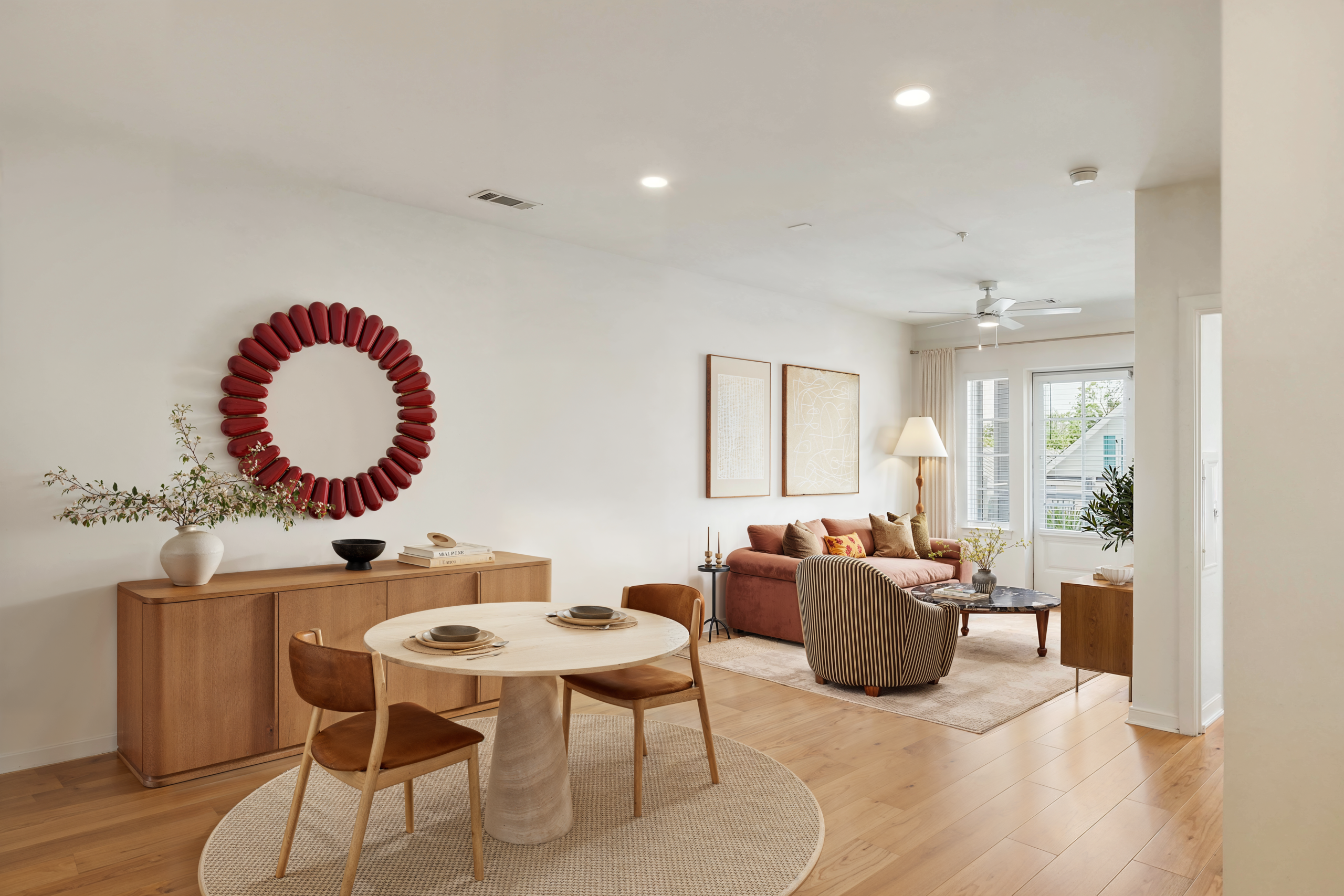 Open-concept dining and living room with round dining table, modern furniture, wood flooring, natural light, and contemporary décor.