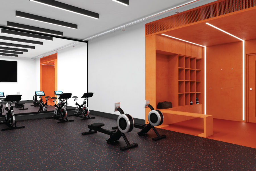 A modern, high-contrast fitness center interior with a bold orange and white color palette. The room features professional-grade black rowing machines and stationary bikes arranged on a dark, speckled athletic floor. A large floor-to-ceiling mirror spans the left wall, reflecting the equipment and a row of sleek, black linear ceiling lights. To the right, a vibrant, deep orange recessed alcove contains custom wooden cubbies and a built-in bench, illuminated by integrated vertical LED light strips. The design is clean, minimalist, and high-energy, reflecting a premium, active lifestyle within a professional residential or office development.