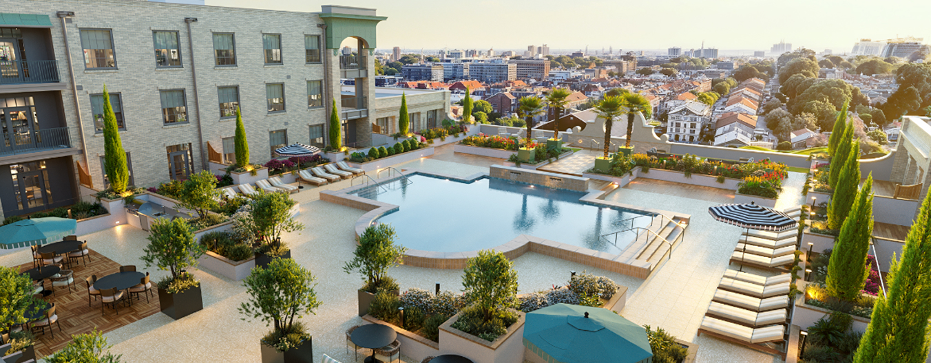 An elevated wide-angle view of the expansive rooftop pool deck at The Laurel during the golden hour. The centerpiece is a large, uniquely shaped swimming pool surrounded by a light-colored stone patio. The deck is meticulously landscaped with tall, slender cypress trees and lush potted greenery. Luxury amenities include rows of tan lounge chairs with striped umbrellas, several outdoor dining sets with teal umbrellas, and a raised wooden terrace area. The pool overlooks a sprawling metropolitan neighborhood, capturing a high-end, resort-style living experience in the heart of the city.