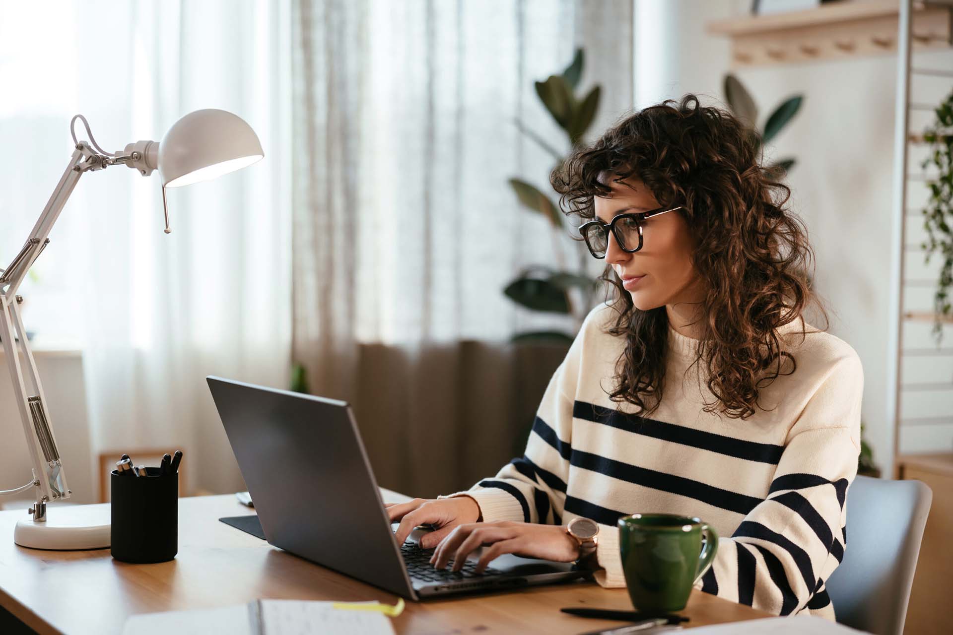 Person in striped sweater and glasses working on laptop computer at desk.