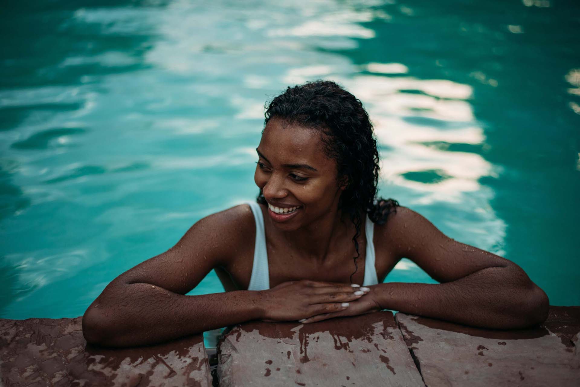 Person in swimming suit smiling and relaxing in a shimmering blue pool.