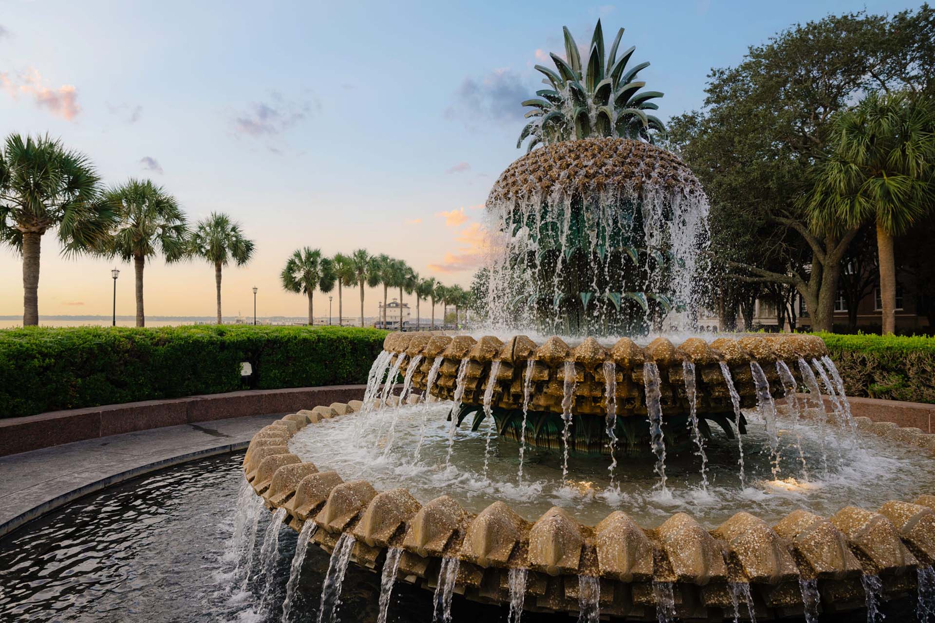 Pineapple shaped fountain near rows of tall palm trees.
