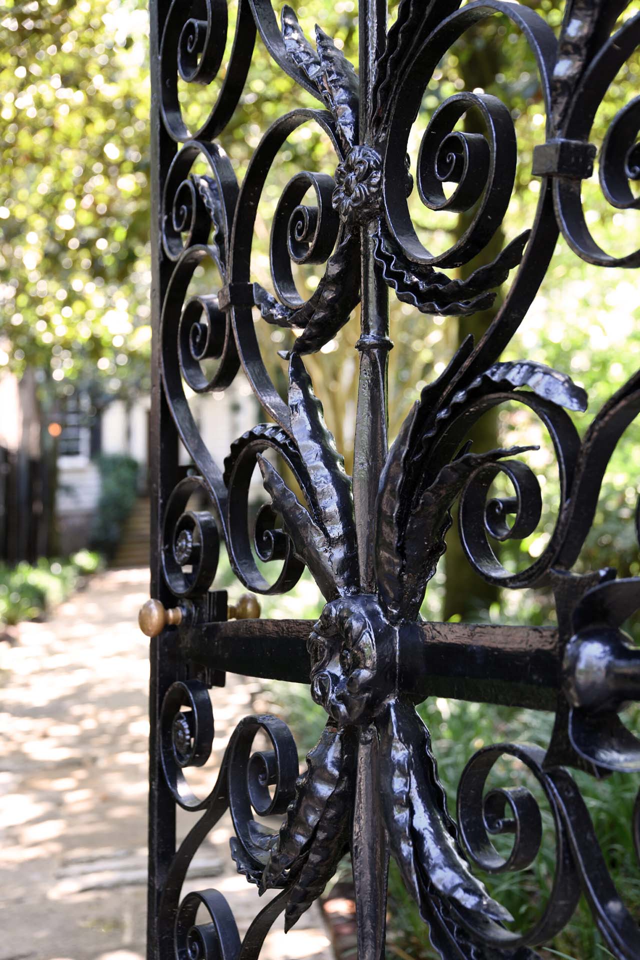 An ornate black metal gate opening to a garden.